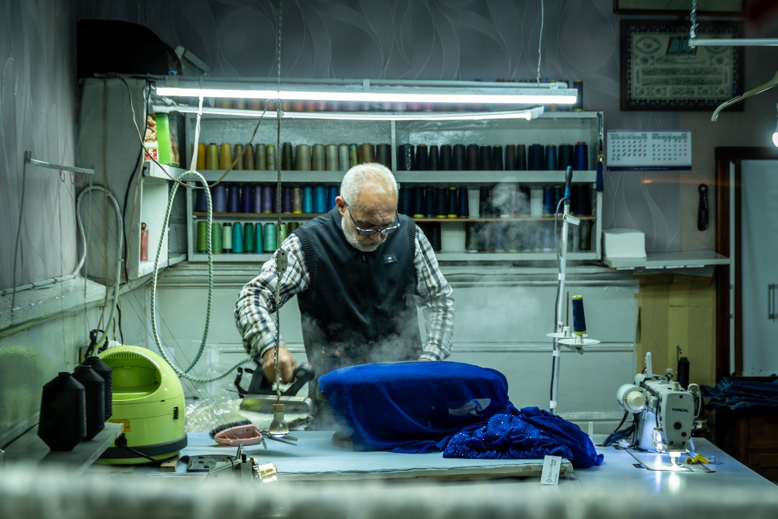 Tailor pressing blue fabric in a workshop as an illustration of controlled tailoring heat and pressure